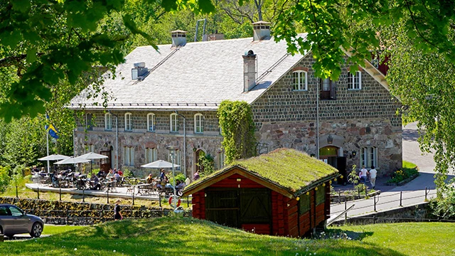En större tegelbyggnad med en uteservering längs långsidan samt en gräsmatta i förgrunden