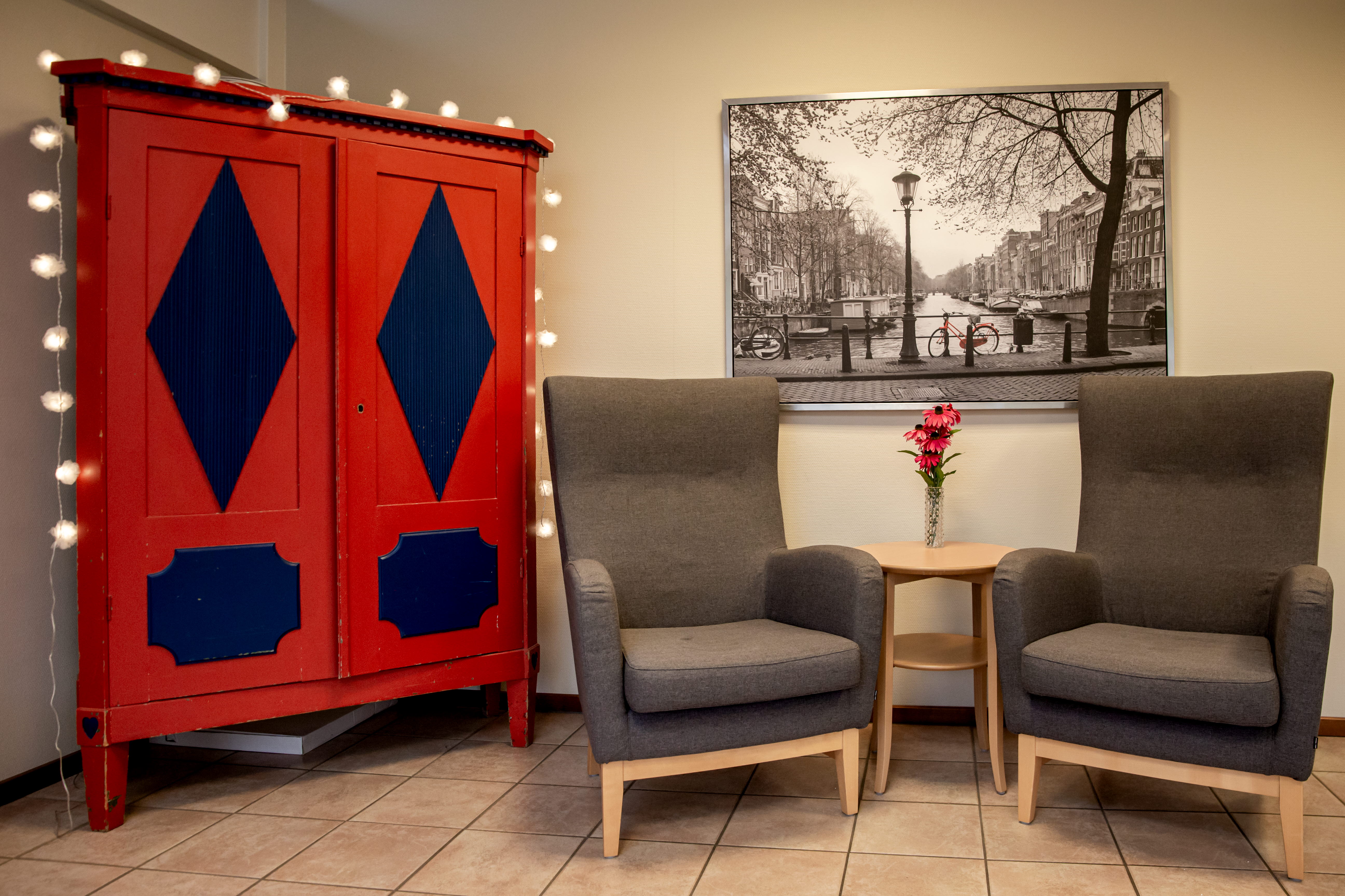 Två fåtöljer med ett lite cafébord samt ett skåp i traditionell stil som är målat rött och blått