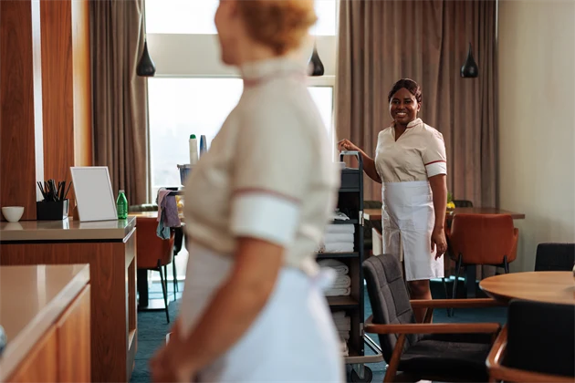 Två hotellanställda personer arbetar i ett konferensrum med en städvagn.