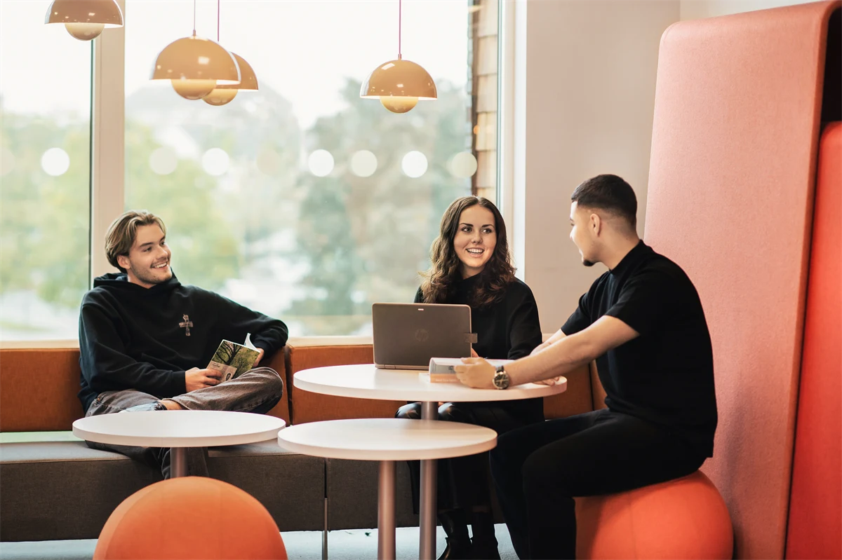 Tre gymnasieelever sitter i en soffa och ler.