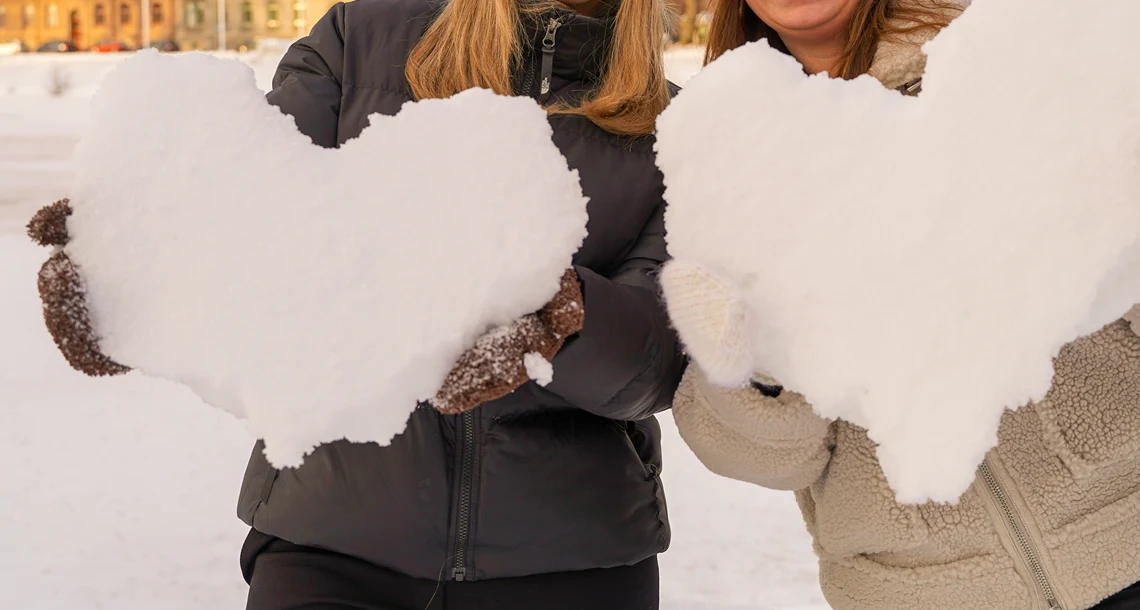 Två tjejer håller hjärtan av snö