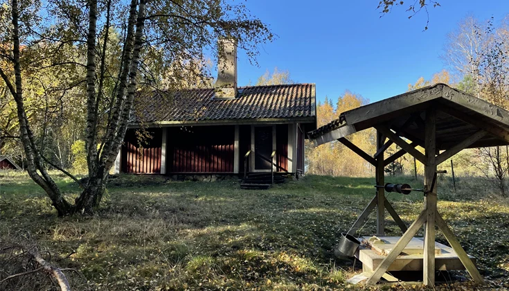 Gammaldags brunn med tak över och en liten röd stuga i bakgrunden.