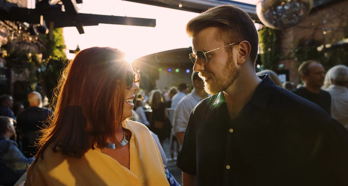 Tjej och kille med solglasögon och solglitter, publik och scen i bakgrunden.