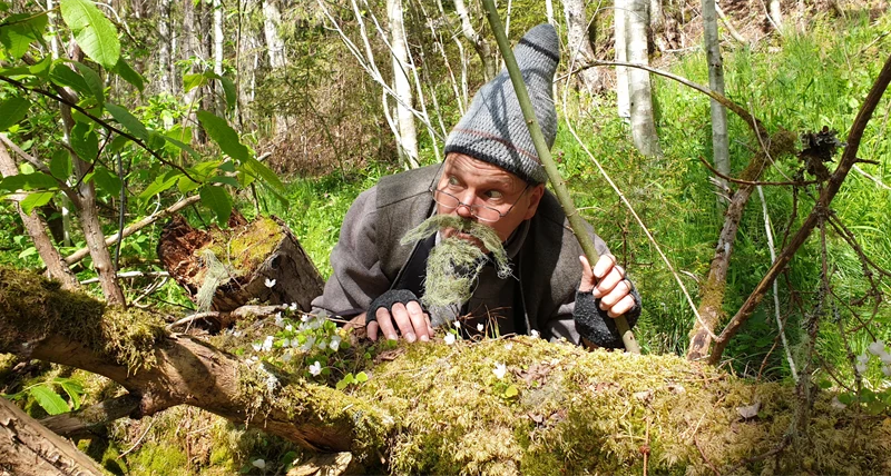 Skådespelare gestaltar en vätte som kikar fram bakom en trädstam.