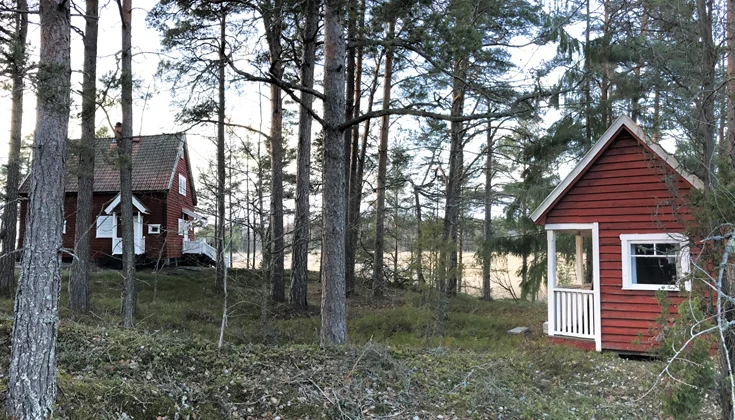 Två röda stugor omgivna av natur