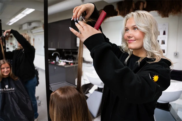 Frisörelev sköljer ur färg ur håret på en kund