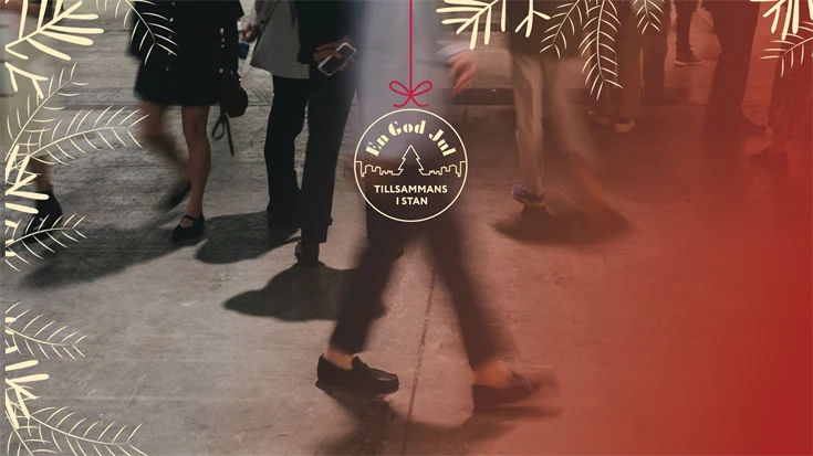 Folkvimmel på en gata.  En illustration av en julkula med texten "En god jul tillsammans i stan".