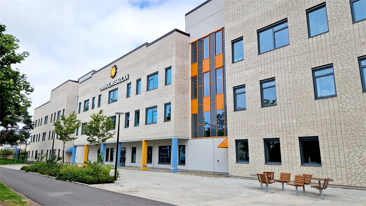 Orrholmsskolan sedd från framsidan, byggnad i ljust tegel i flera våningar med färgglada pelare i bottenplan