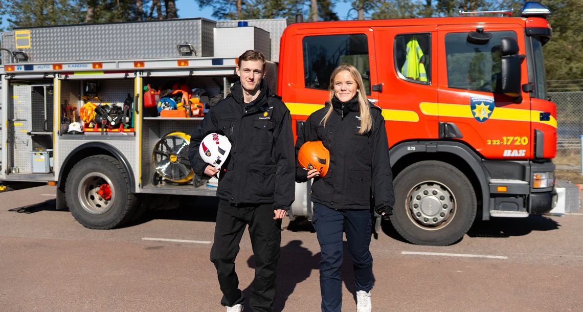 Två personer går framför en parkerad brandbil.