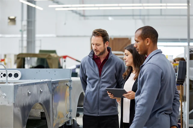 Tre personer tittar på en produkt i metall i en verkstad.