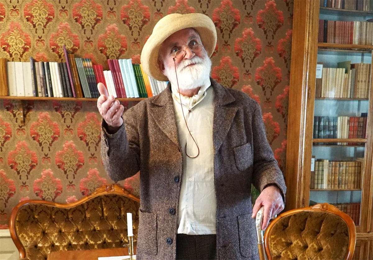 Skådespelare efterliknande Gustaf Fröding i 50-årsåldern står i Frödingbiblioteket och gestikulerar. 