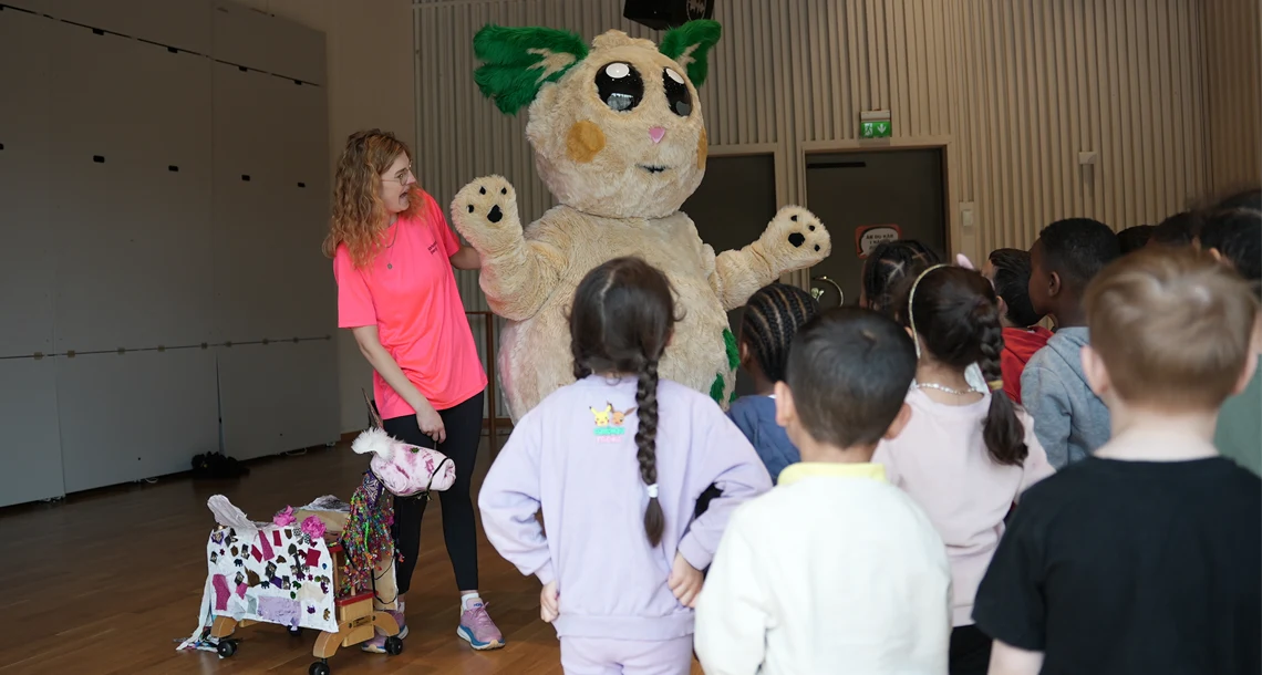 Barn som står runt en person utklädd till maskot.