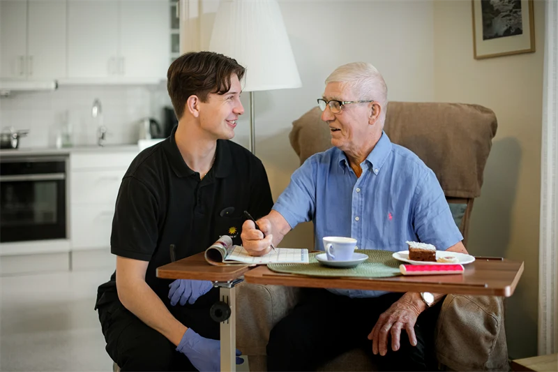 En yngre man inom vård och omsorg hjälper en äldre man. 