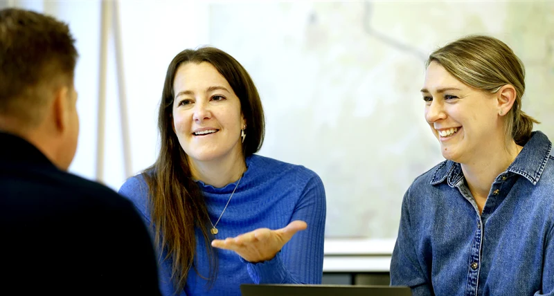 Två kvinnor gestikulerar och pratar med man som man endast ser ryggen på.