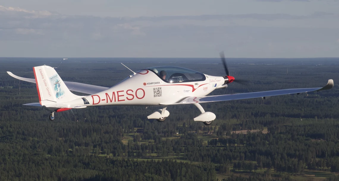 Ett mindre flygplan i luften. Man ser planet flyga över ett stort skogsområde och även en horisontlinje.