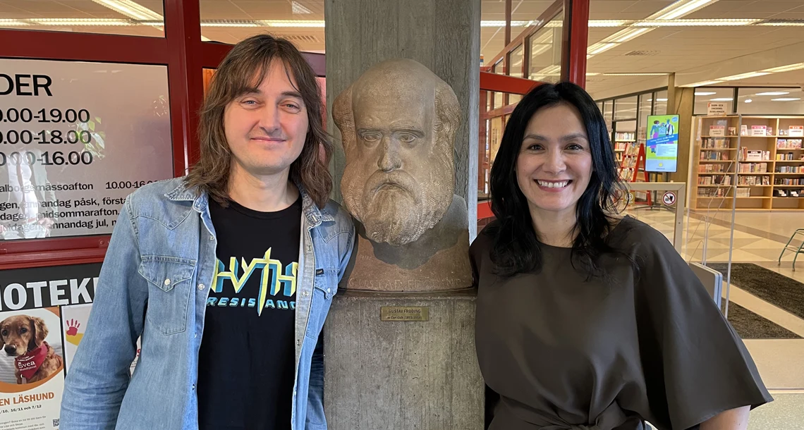 Porträttfoto av man och kvinna på var sida om en skulptur