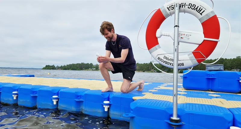 Vattenprov har tagits från brygga. Miljöinspektören står på knä med provflaska i handen.