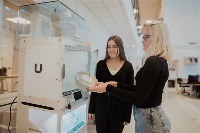 Två personer vid en maskin. Den ena tar ut ett föremål ur maskinen.