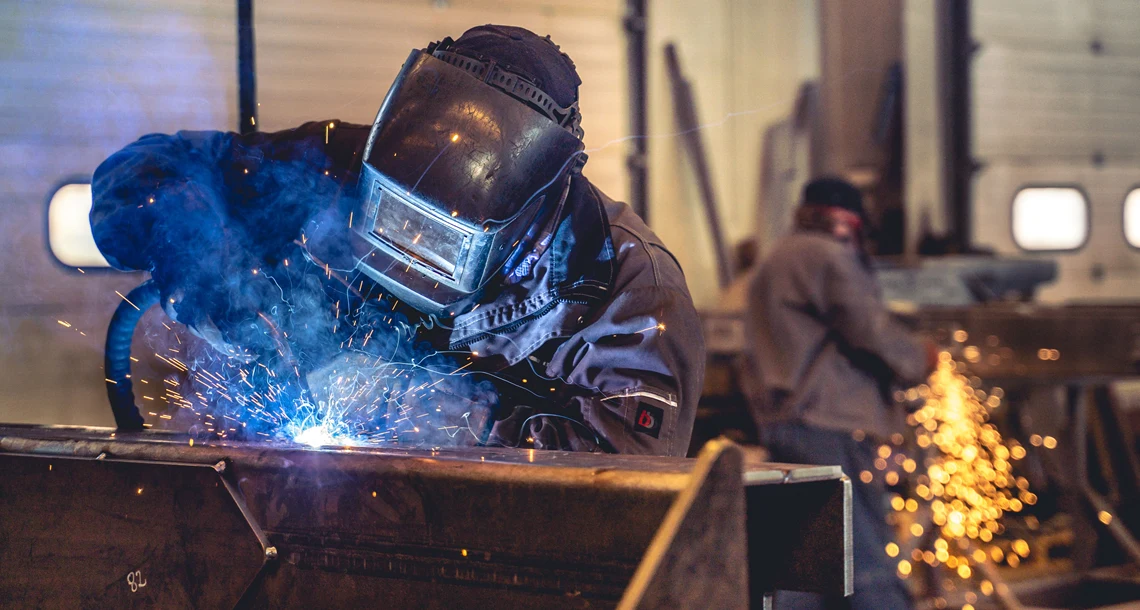 Två personer med svetsutrustning svetsar.