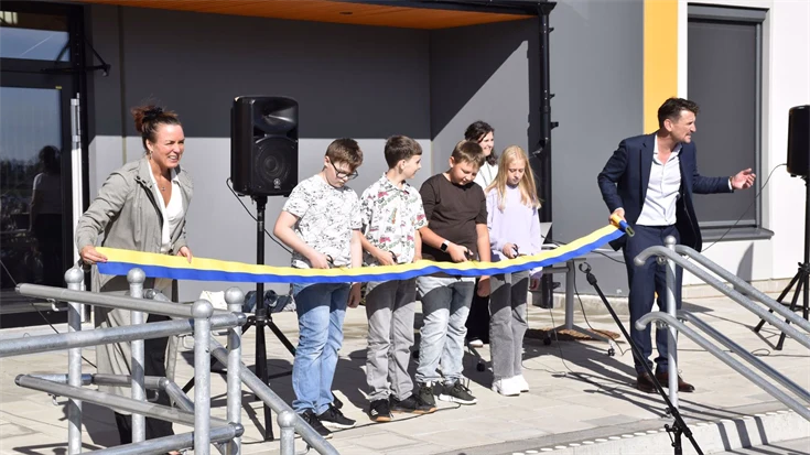 Elever och vuxna som klipper ett blågult band framför en skolbyggnad