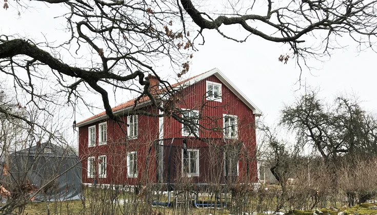 Ett rött trähus med vita knutar omgivet av en trädgård