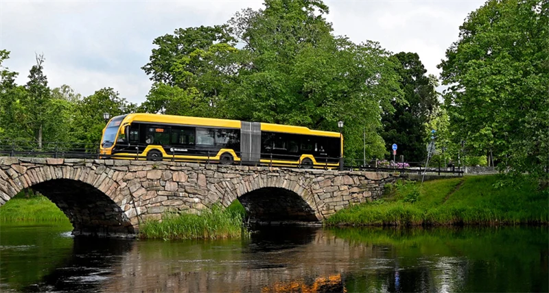En gul buss åker över stenbro med valv.