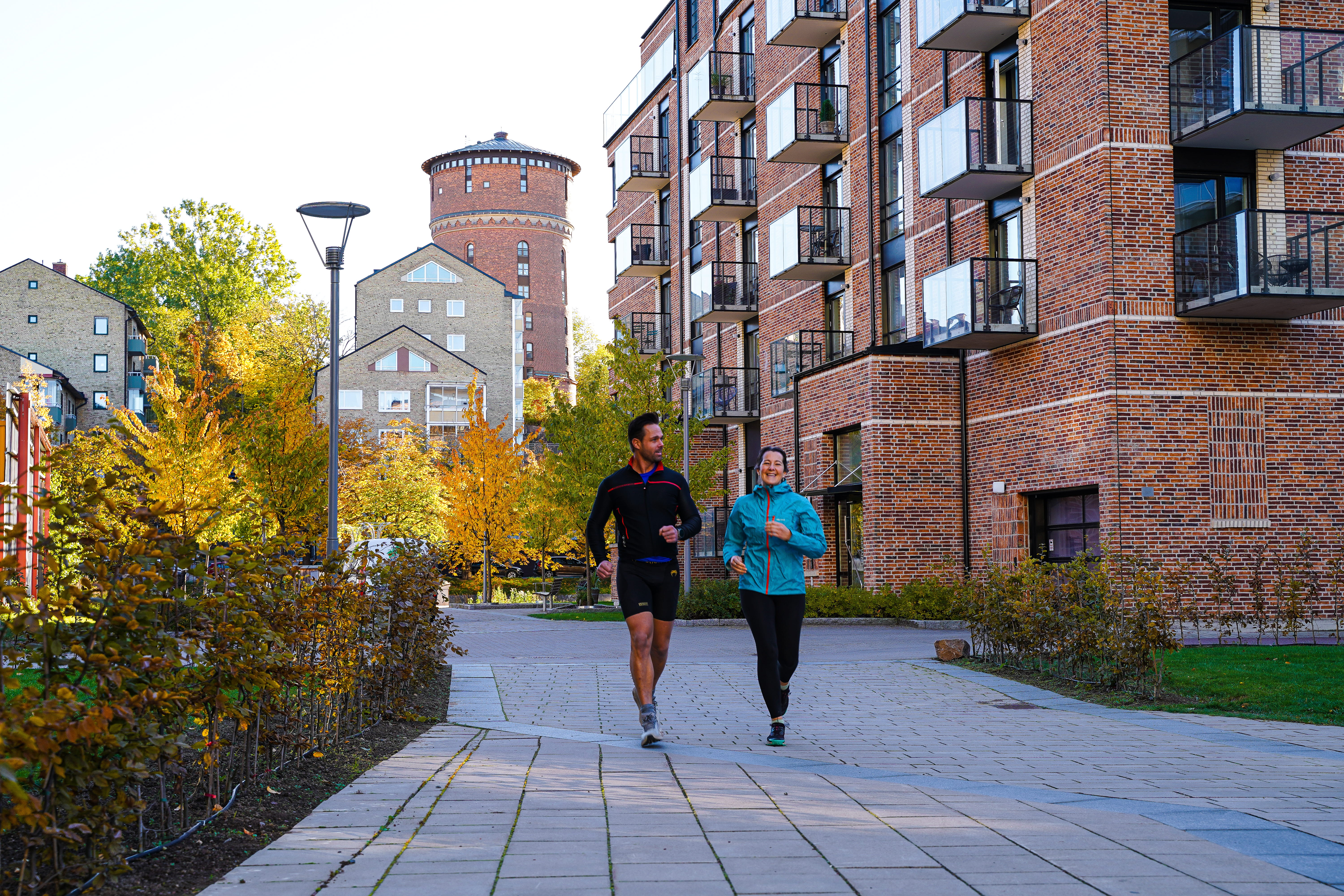 Två personer joggar utomhus, i bakgrunden syns både grönska och tegelhus.