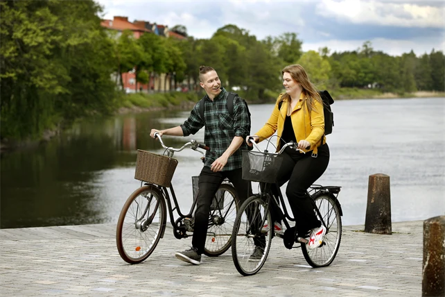 En kille leder sin cykel medan en tjej cyklar bredvid