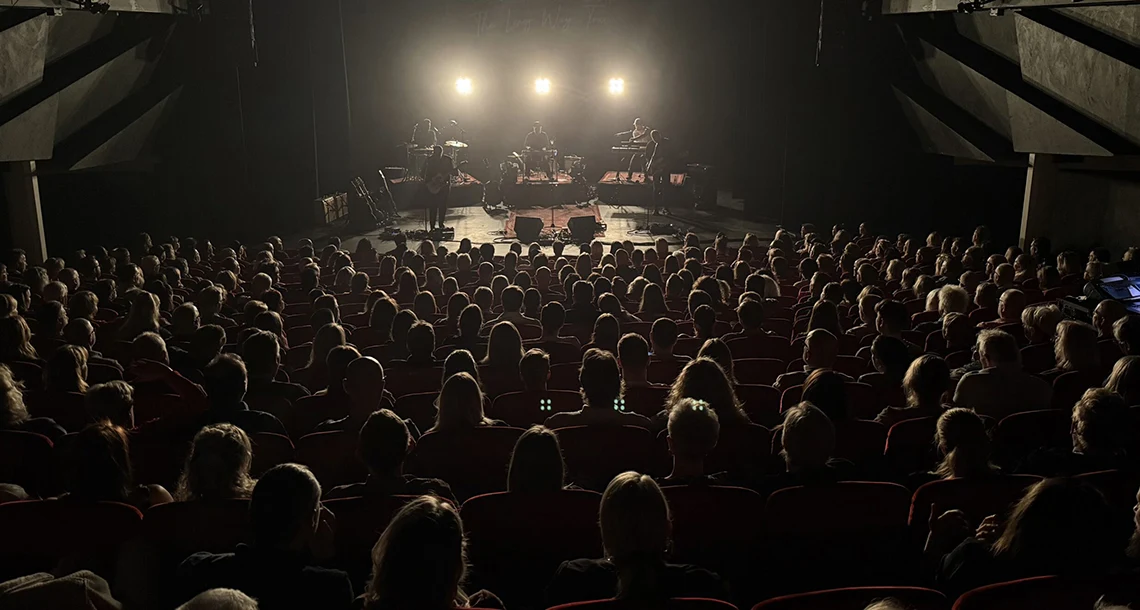 Ett band är på en nedsläckt scen och spelar musik inför sittande människor