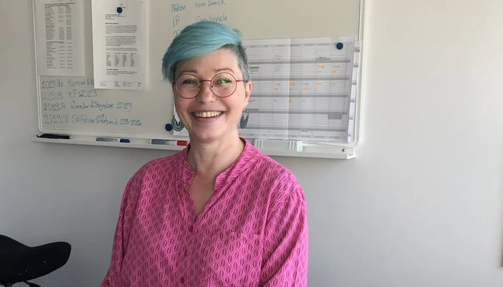 Kvinna sitter bakom ett skrivbord och ler mot kameran.