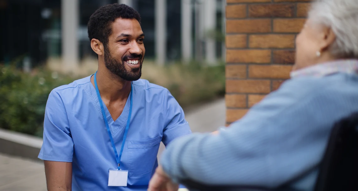 En person sitter på knä och ler mot en person som sitter i rullstol.